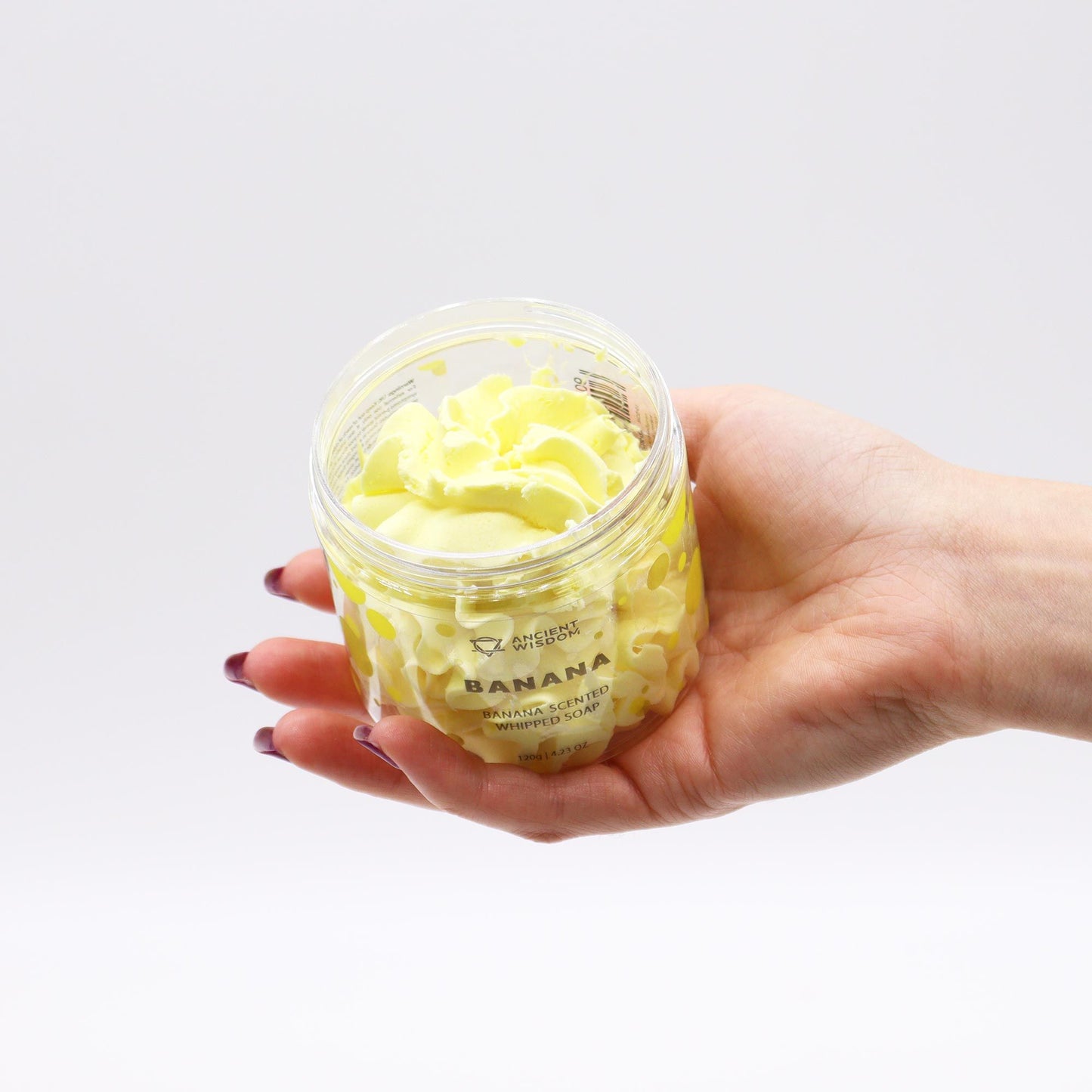 A hand holding a jar of Banana Whipped Soap 120g showcasing its creamy texture, perfect for skincare. A fantastic option for a vegan, cruelty-free Christmas Gift Home Fragrance.