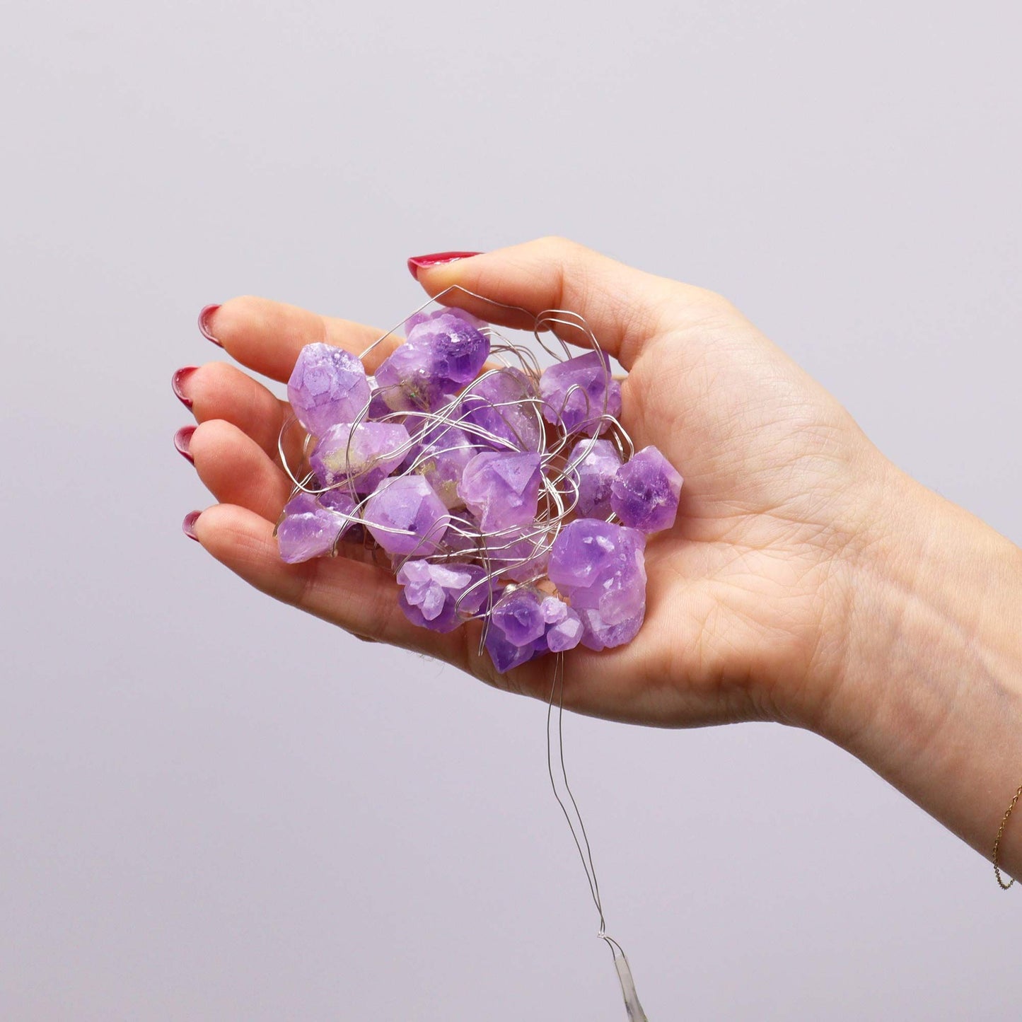 A hand holding the Amethyst Gemstone Enchantment LED String Lights, showcasing the beautiful purple crystals, ideal for creating a calming atmosphere in your home or as a thoughtful gift.