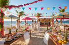 A vibrant beach scene showcasing beach party essentials like colourful decor, delicious food tables, and guests celebrating under umbrellas during a summer beach party.