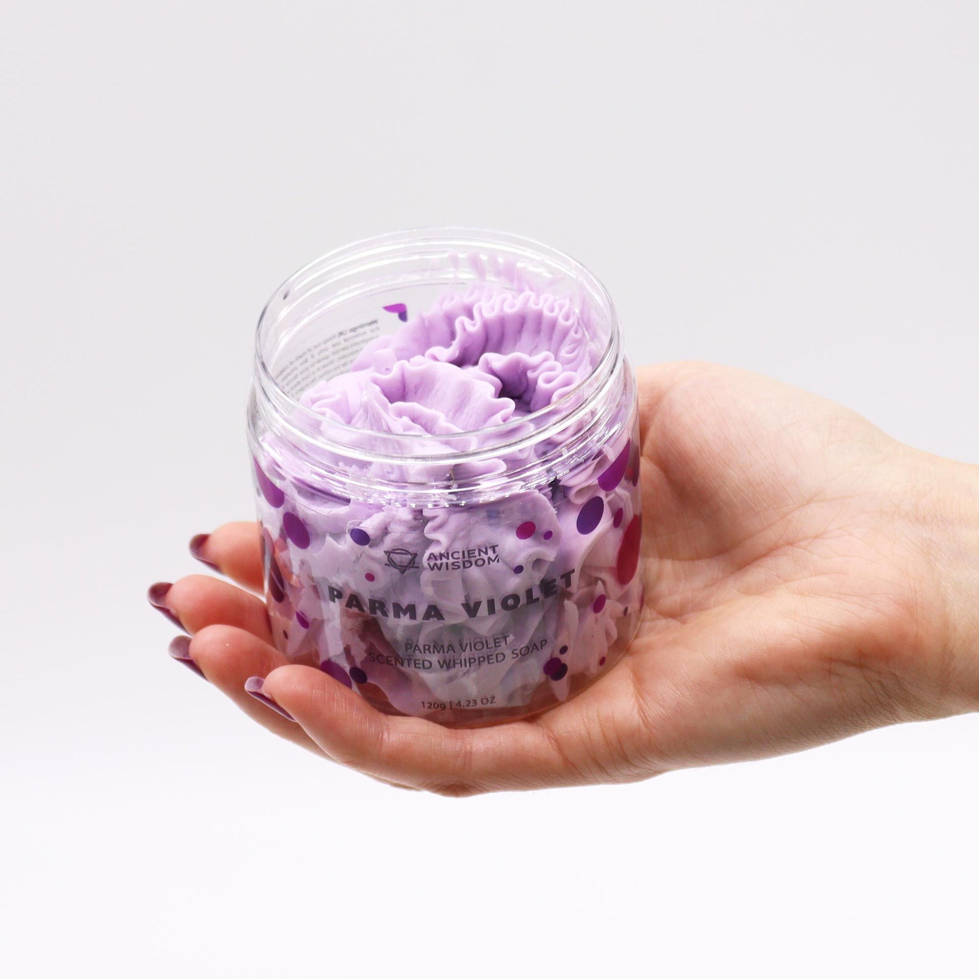 A hand holding a jar of Parma Violet Whipped Soap 120g, showcasing its creamy, velvety texture and captivating purple colour. This luxurious vegan bath indulgence is an ideal Christmas gift home fragrance.