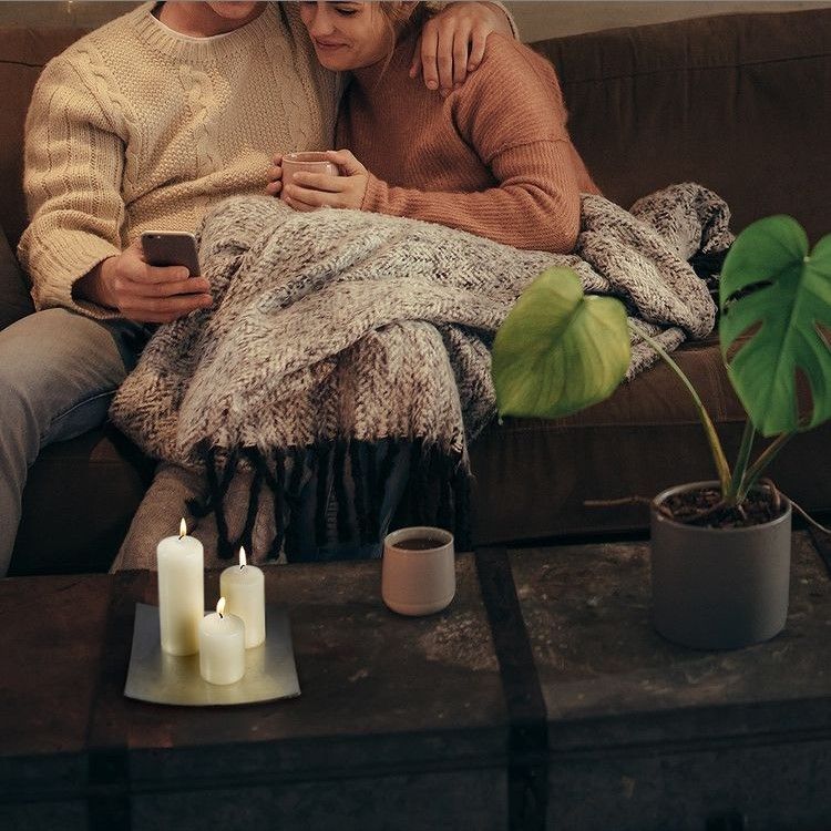 Ivory Pillar Candle 60x120mm – 38h Burn Time, Perfect for Home, featured in a cozy living room setting with a couple enjoying a moment together, emphasizing its role as a Christmas Gift Home Fragrance.