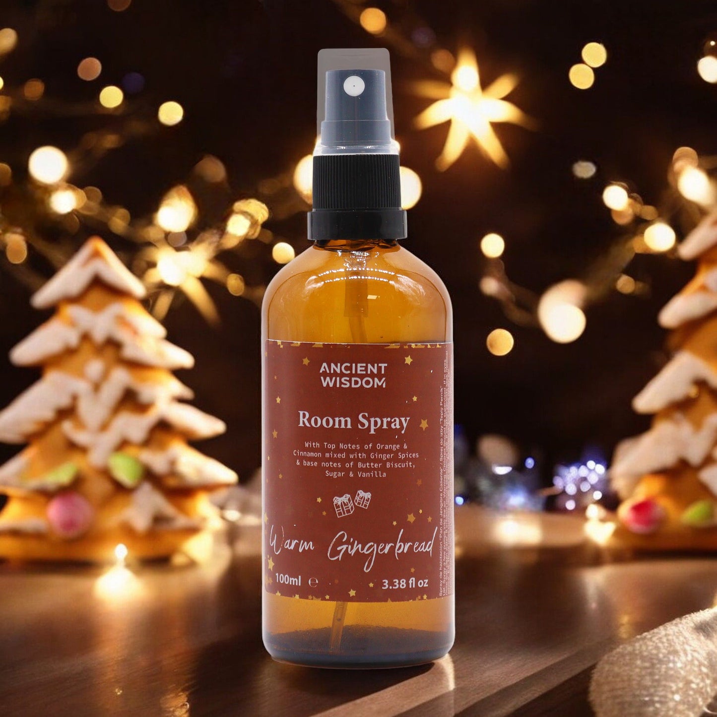 Warm Gingerbread Room Spray 100ml displayed with a festive background of twinkling lights and gingerbread houses. An ideal Christmas gift or stocking filler, this fragrant delight offers a nostalgic blend of cinnamon orange and other winter spices, making it a perfect choice for enhancing home ambiance and self-care with aromatic bliss.