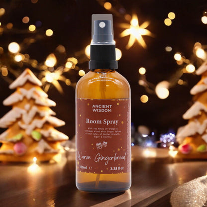 Warm Gingerbread Room Spray 100ml displayed with a festive background of twinkling lights and gingerbread houses. An ideal Christmas gift or stocking filler, this fragrant delight offers a nostalgic blend of cinnamon orange and other winter spices, making it a perfect choice for enhancing home ambiance and self-care with aromatic bliss.
