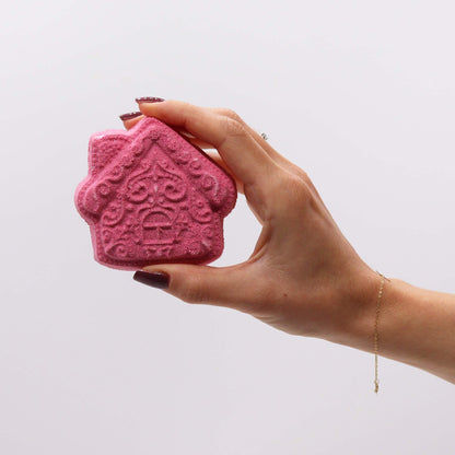 Close-up of a pink gingerbread house bath bomb from the Gingerbread Town Christmas Bath Bomb Gift Pack, held in a hand. Exuding the lovely Warm Gingerbread scent – ideal for Christmas gift home fragrance.