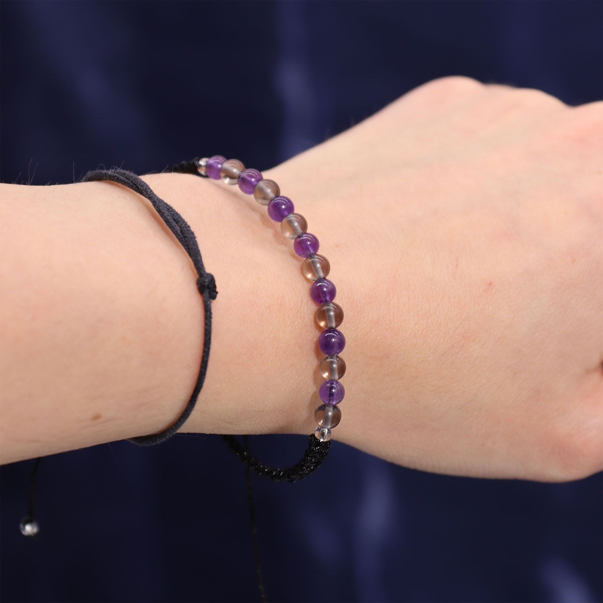 A close-up of a hand wearing a beautifully crafted gemstone bracelet featuring Amethyst and Smoky Quartz. This elegant accessory accompanies the Zodiac Crystal Candle with Gemstone Bracelet - Capricorn, offering a serene blend of style and astrology. Ideal as a Christmas gift, this home fragrance adds a touch of luxury to any space.