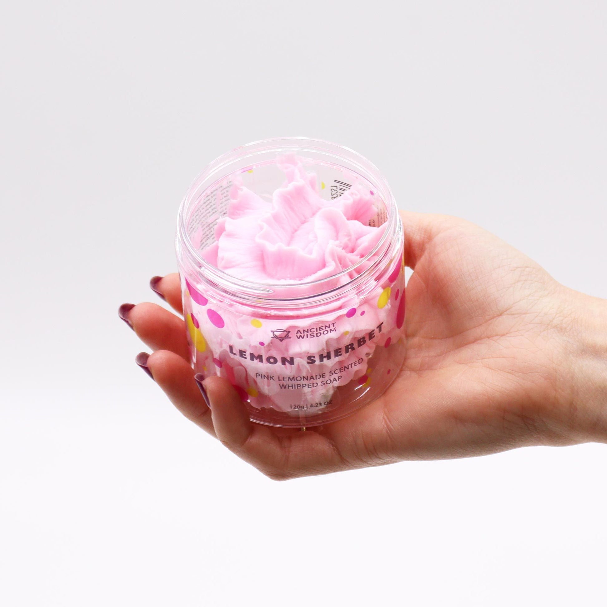 Hand holding a jar of Pink Lemonade Whipped Soap 120G, revealing its creamy, pink texture. This vegan, moisturising treat offers a sweet scent, perfect as a Christmas gift for lovers of home fragrance.