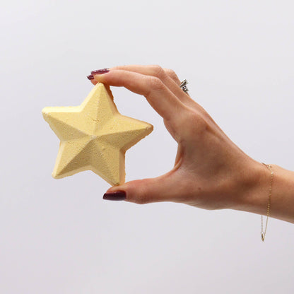 Christmas Wish List Christmas Bath Bomb Gift Pack featuring a yellow star bath bomb in a hand. An excellent addition to any holiday bath, this star-shaped bath bomb offers a delightful scent and serves as a lovely Christmas gift.
