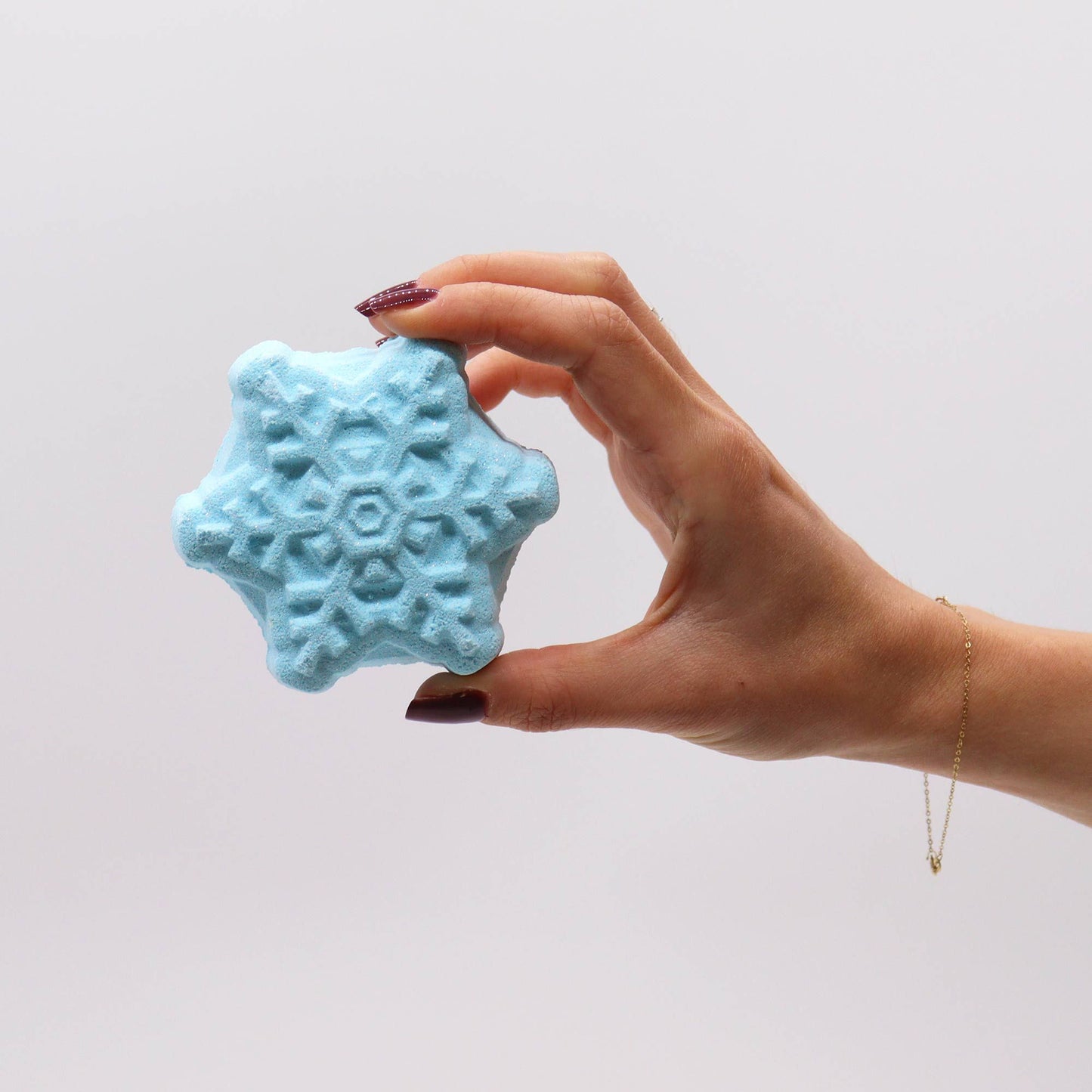 Hand holding a blue snowflake bath bomb from the Break the Ice Christmas Bath Bomb Gift Pack, highlighting its charming details. An excellent option for Christmas gifting and delightful home fragrance.