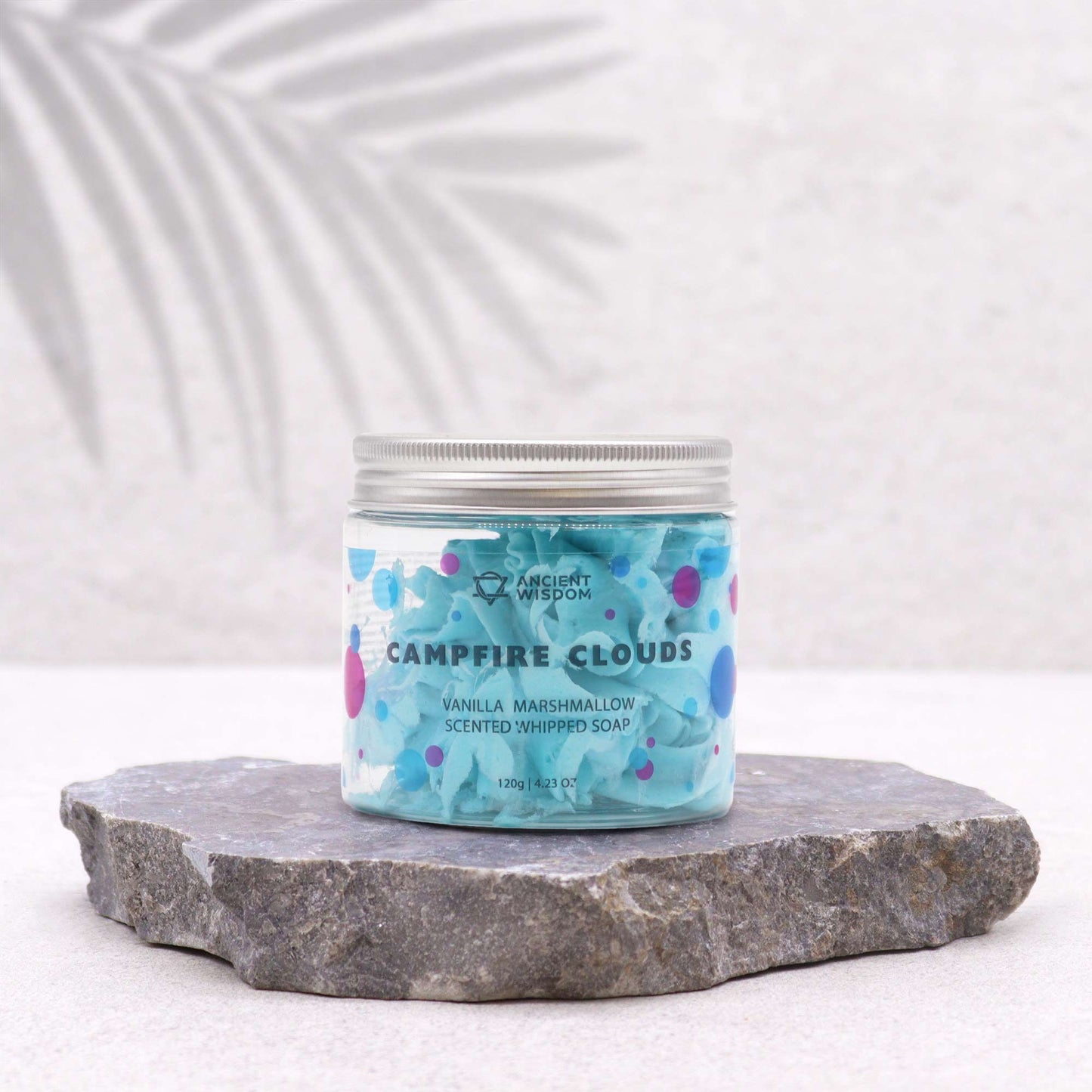 Campfire Clouds Marshmallow Whipped Soap 120g displayed on a natural stone surface, showcasing its charming packaging with a blue hue and colourful dots. A lovely choice for a Christmas gift home fragrance for pampering moments.