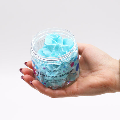 Hand holding a jar of Marshmallow Whipped Soap 120g, revealing its fluffy whipped texture in a bright blue. A luxurious scented soap that doubles as a delightful Christmas gift home fragrance for those cozy bath times.