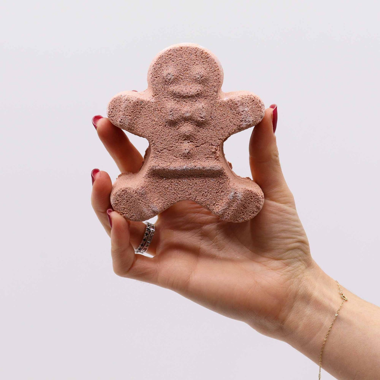 A hand holding a gingerbread man-shaped bath bomb from the Christmas Fun Bath Bomb Gift Pack. Warm Gingerbread scent, perfect for holiday relaxation and festive joy, making it a delightful Christmas Gift Home Fragrance.