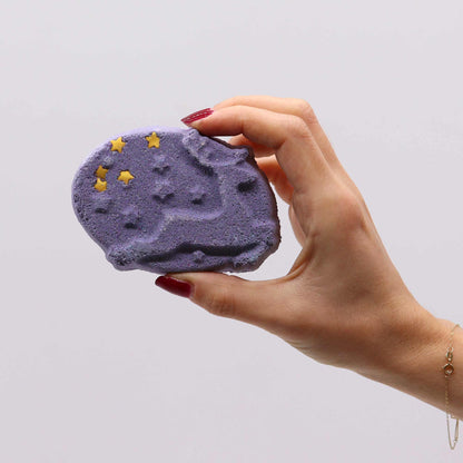 A hand showcasing a purple ice skate-shaped bath bomb from the Christmas Fun Bath Bomb Gift Pack. Frosted Sugar Plum scent adds a festive touch, ideal for creating a cheerful atmosphere, perfect as a Christmas Gift Home Fragrance.
