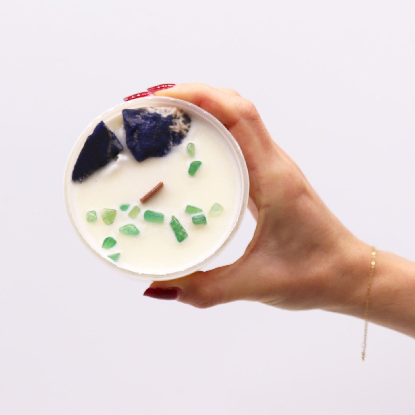 A hand holding the Throat Chakra Candle with Sodalite & Jade. With its soothing fragrance of Gentle Reasons, this {{scent}} {{product_type}} is a lovely Christmas Gift Home Fragrance.