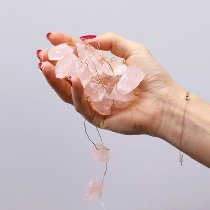 A hand holding strands of Rose Quartz Gemstone Enchantment Lights, illustrating their delicate design and versatility as a lovely Christmas gift to brighten up any home.