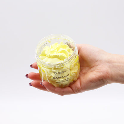 A hand holding a jar of Banana Whipped Soap 120g showcasing its creamy texture, perfect for skincare. A fantastic option for a vegan, cruelty-free Christmas Gift Home Fragrance.