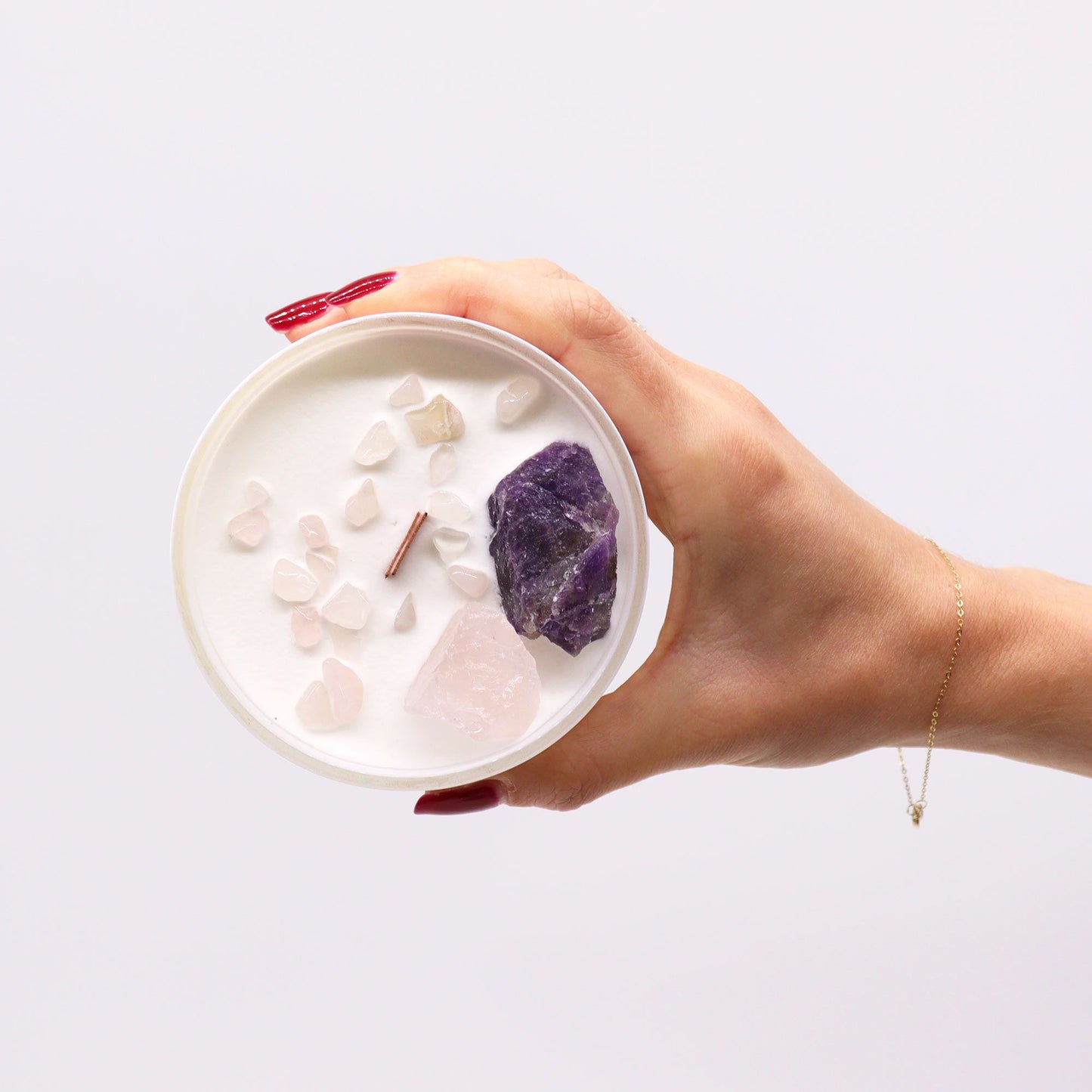A hand holding the Third Eye Chakra Candle – Enhance Intuition & Inner Wisdom, displaying Amethyst and Rose Quartz crystals on top. A charming home fragrance, ideal for Christmas gifting.