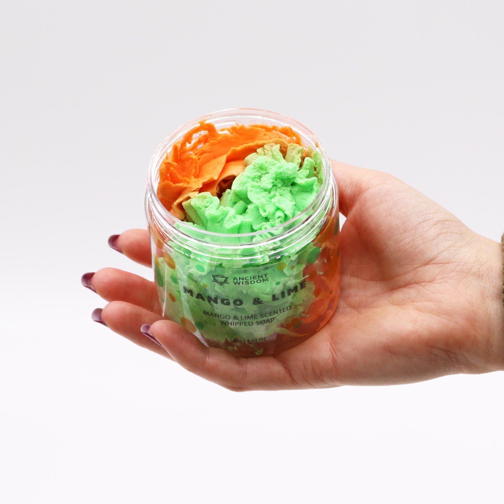 A hand holding a jar of Tropical Mango & Lime Whipped Soap 120g, displaying the colourful layers of green and orange whipped soap. This luxurious vegan soap makes for a delightful Christmas gift, perfect for enhancing your home fragrance with refreshing mango and lime aromas.