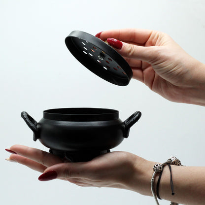A hand holding the lid of the Mystical Cast Iron Cauldron Incense Burner, highlighting its practical use and enchanting design. This unique home décor piece is a perfect Christmas Gift Home Fragrance for those who appreciate mystical touches.