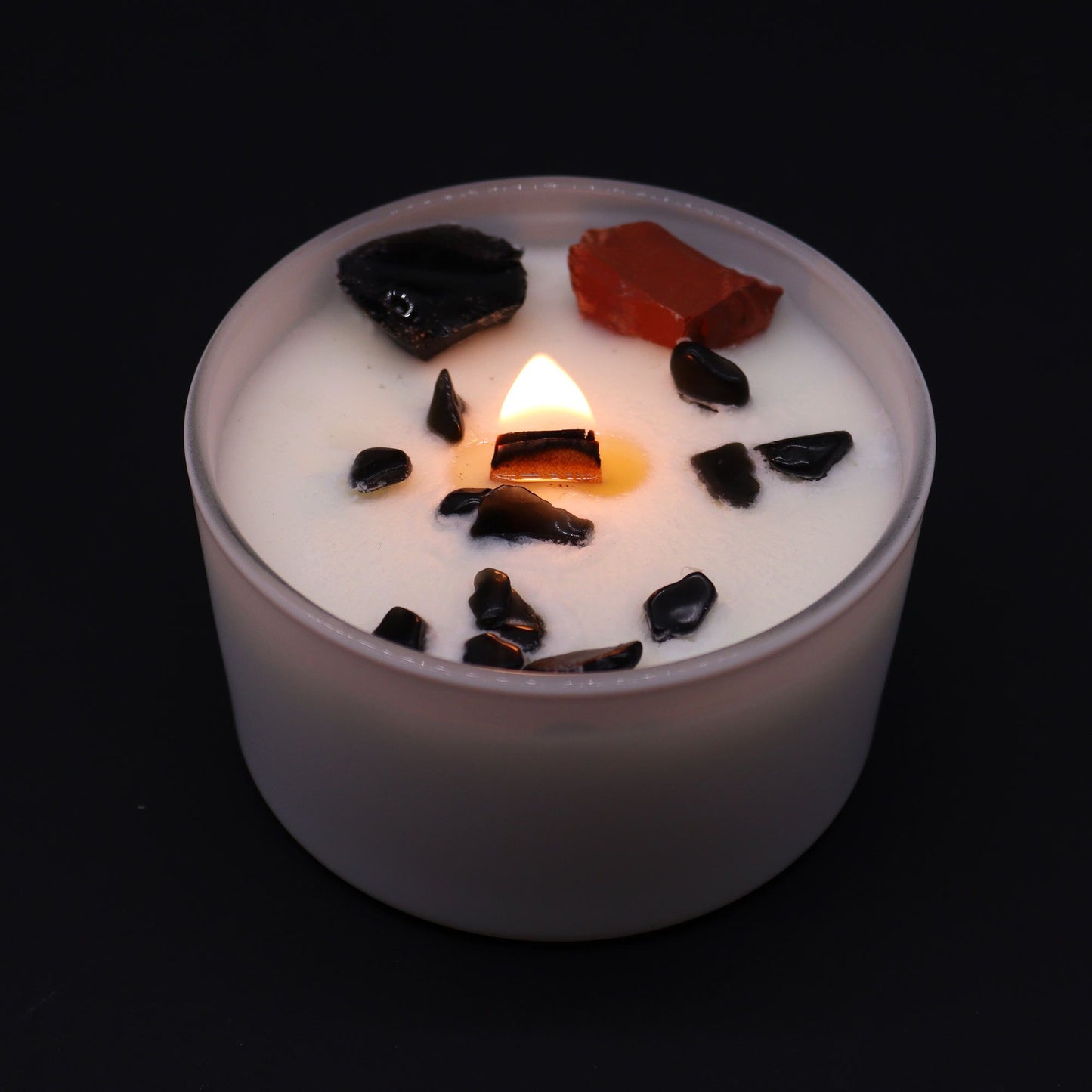 Root Chakra Crystal Candle - Black Oud Scent with Gemstones burning softly, showcasing black and red gemstones on top. A beautiful addition for a relaxing environment and a great Christmas Gift Home Fragrance.