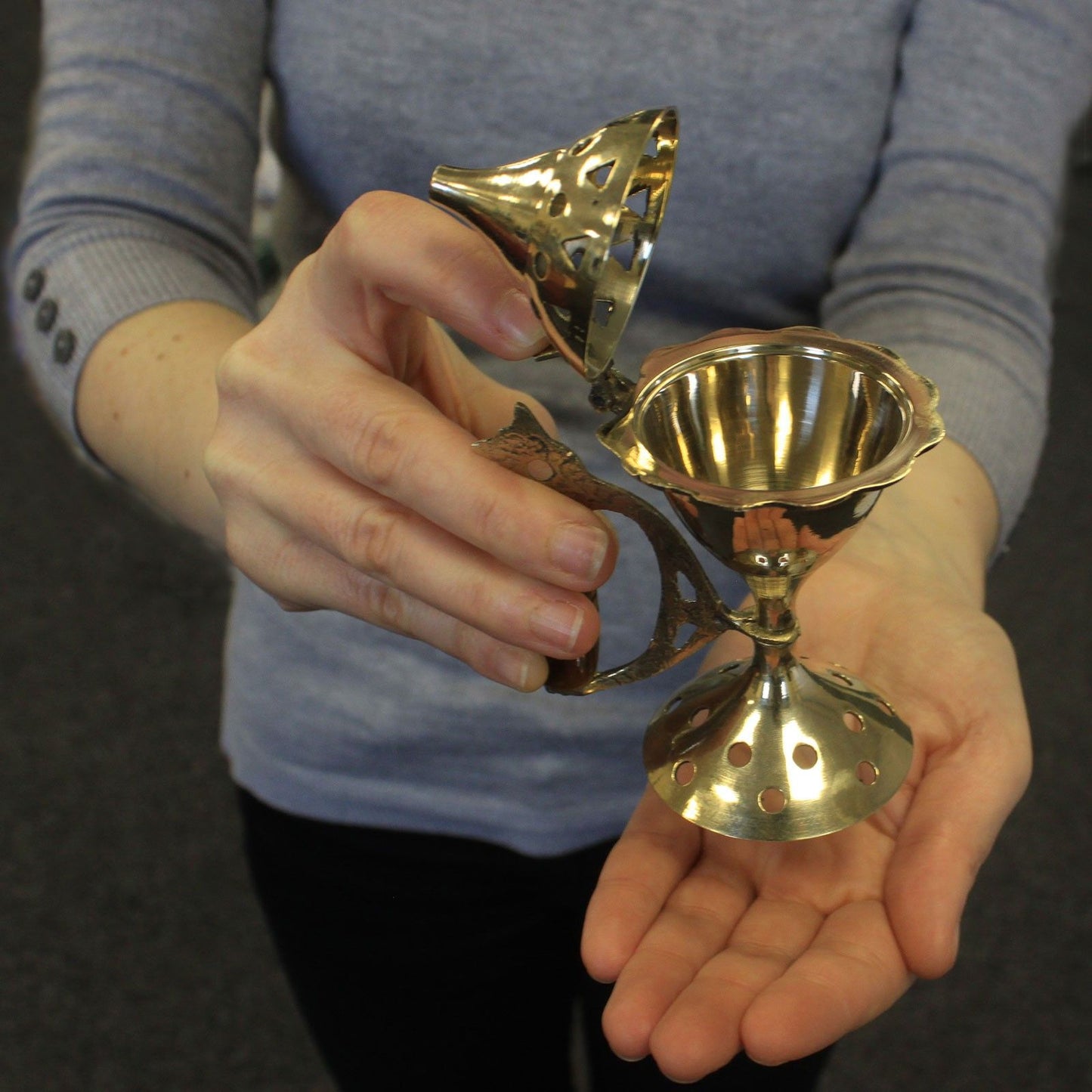 A person holding the Elegant Brass Cone Incense Burner with Carved Handle, showcasing its intricate design, perfect for enhancing your space. Ideal as a Christmas gift for home fragrance lovers.
