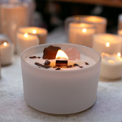 A beautifully lit Sacral Chakra Candle with Tiger Eye and Rose Quartz, radiating a warm glow among other flickering candles. Ideal for nurturing creativity, it makes a great Christmas gift home fragrance.