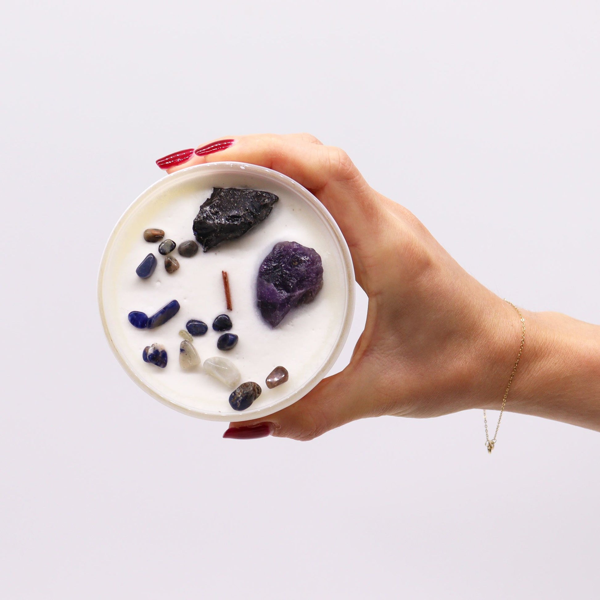 A hand holding the Solar Plexus Chakra Candle adorned with gemstones, including Amethyst and Black Agate, all under the captivating scent of "Deep in the Forest". A stylish way to boost self-confidence and a great Christmas gift for home fragrance lovers.