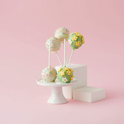 Green-lemon cake pops with floral decorations on a white stand against a pink background
