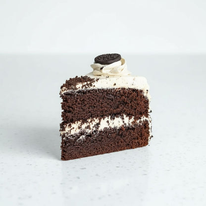 Slice of chocolate cake with cream and Oreo cookie on a light gray background
