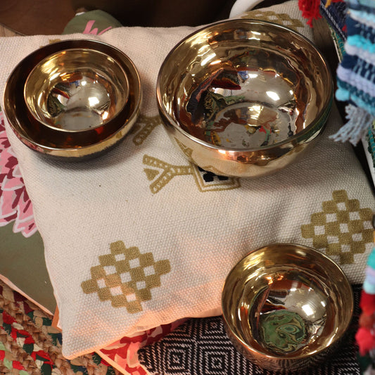 Three sizes of Large Handmade Singing Bowls stacked together on decorative fabric, showcasing their reflective surfaces. Ideal as a Christmas Gift for those seeking home fragrance and relaxation.